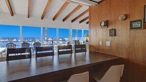 A dining area with a view of the harbor, wooden ceiling beams, and a table with chairs.