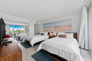 Two single beds with white linens and brown pillows, a flat-screen TV, and a large window offering a view of the outdoors.