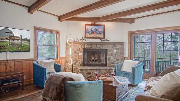 A cozy living room with a stone fireplace, blue upholstered chairs, a wooden coffee table, and a television displaying a scenic view.