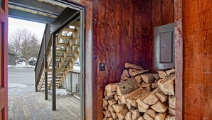 A wooden interior with a stack of firewood and a metal box on the wall.