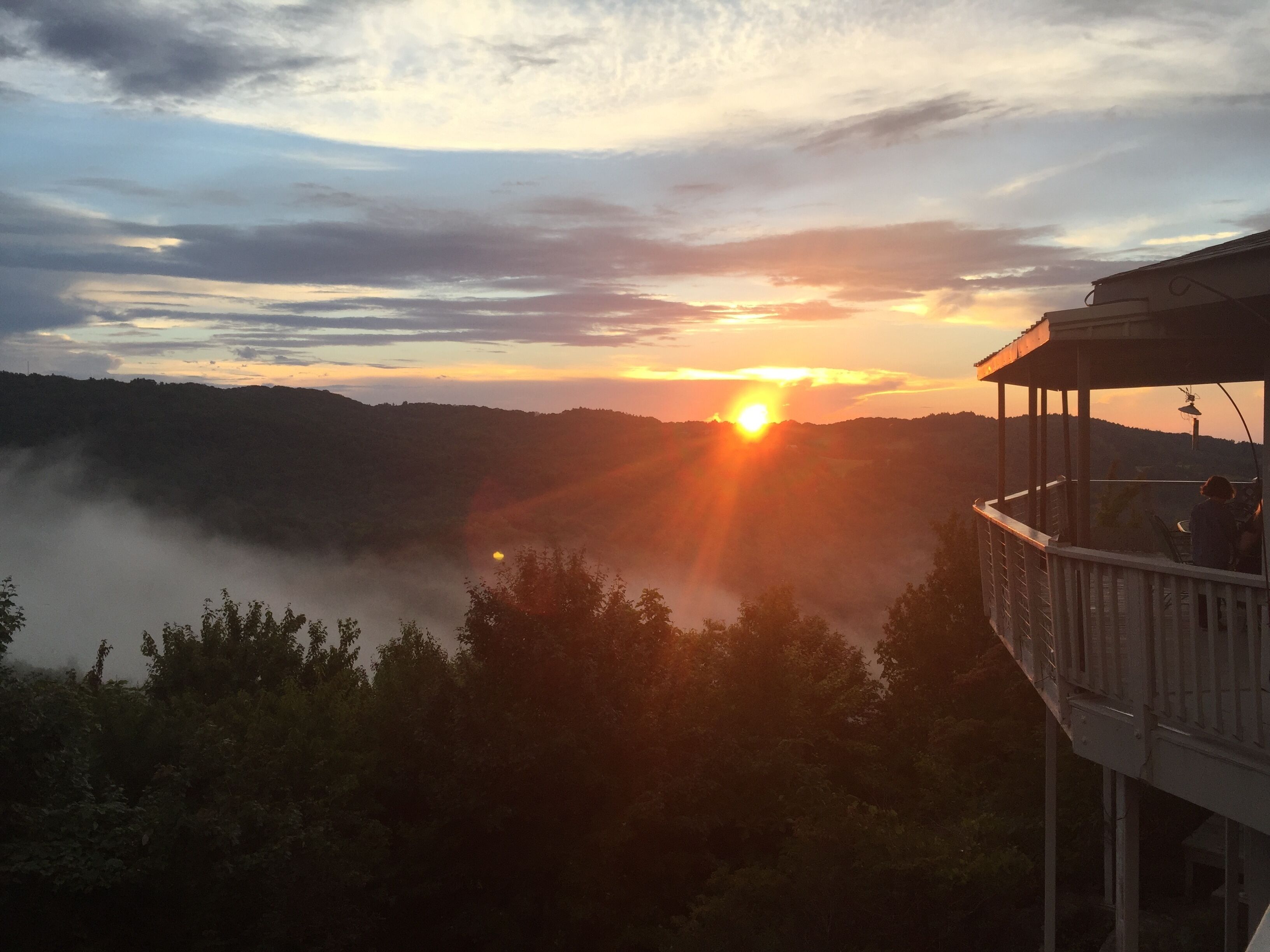 Zonsondergang vanaf een balkon met uitzicht op een vallei met mist en heuvels in de verte.
