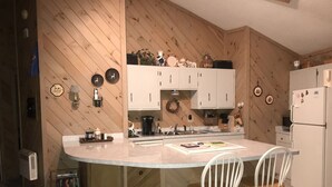 A kitchen with wooden paneling, white cabinets, a central island with two chairs, and various kitchen appliances. - Marvelous Panoramic Mountain Views All Year, Private,Club,Skiing Slopes nearby! (Beech Mountain)