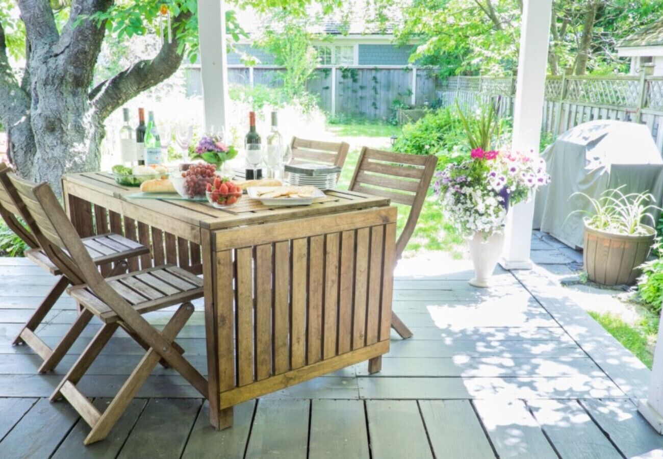 Um deck de madeira com uma mesa e cadeiras, cercado por vasos de plantas e um cercado.