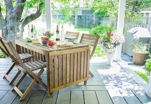 A wooden deck with a table and chairs, surrounded by potted plants and a fence.