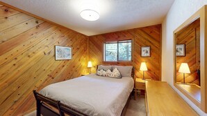 Une pièce chaleureuse aux murs en bois, un lit avec une literie à rayures, deux tables de chevet avec des lampes et des tableaux encadrés accrochés aux murs.