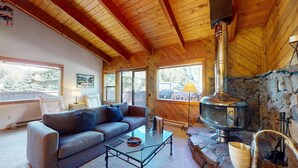 L’intérieur d’un chalet accueillant, avec une cheminée en pierre, un canapé, une table basse et une grande fenêtre.