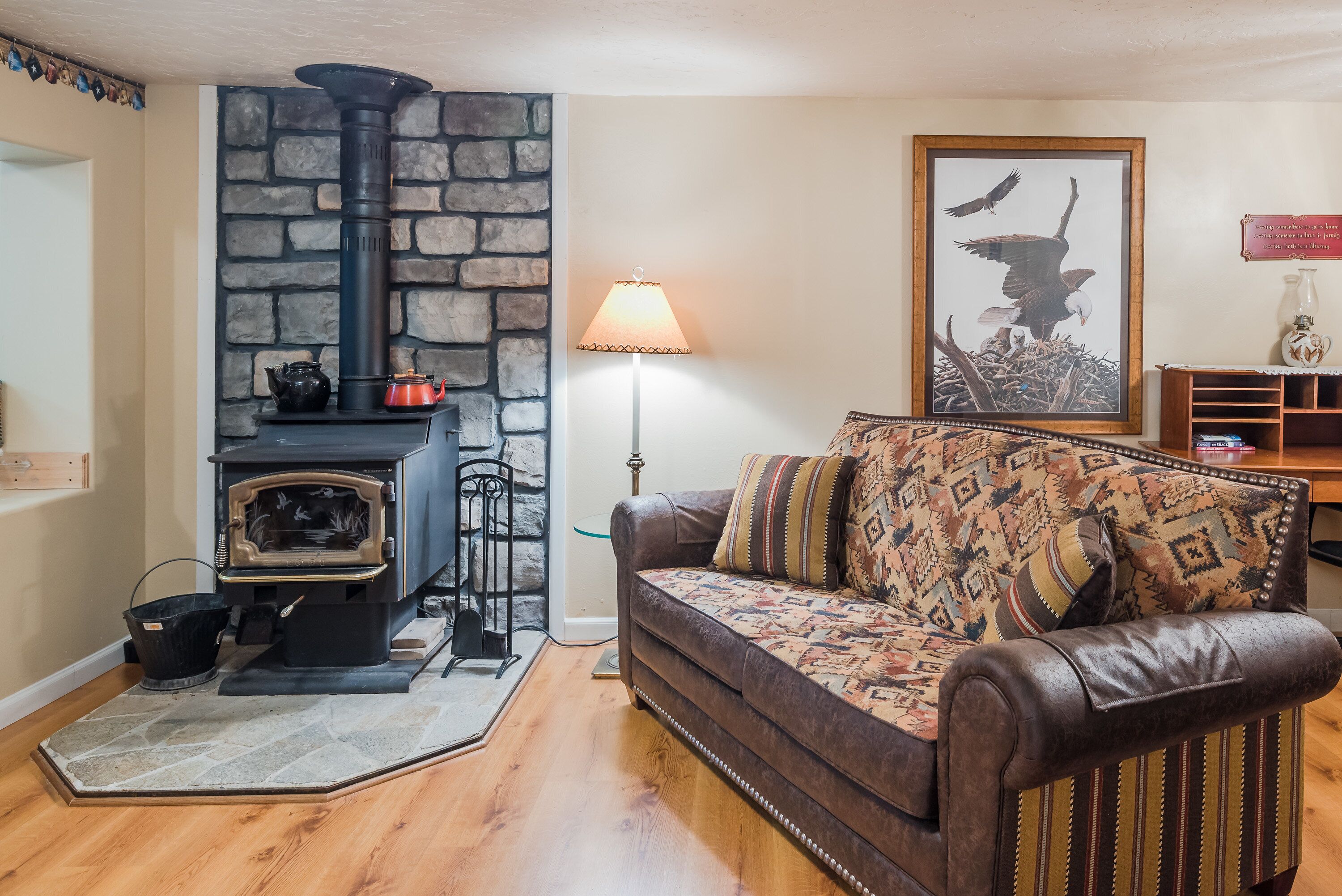 A cozy living room with a stone fireplace, a leather sofa, and a framed picture of an eagle.