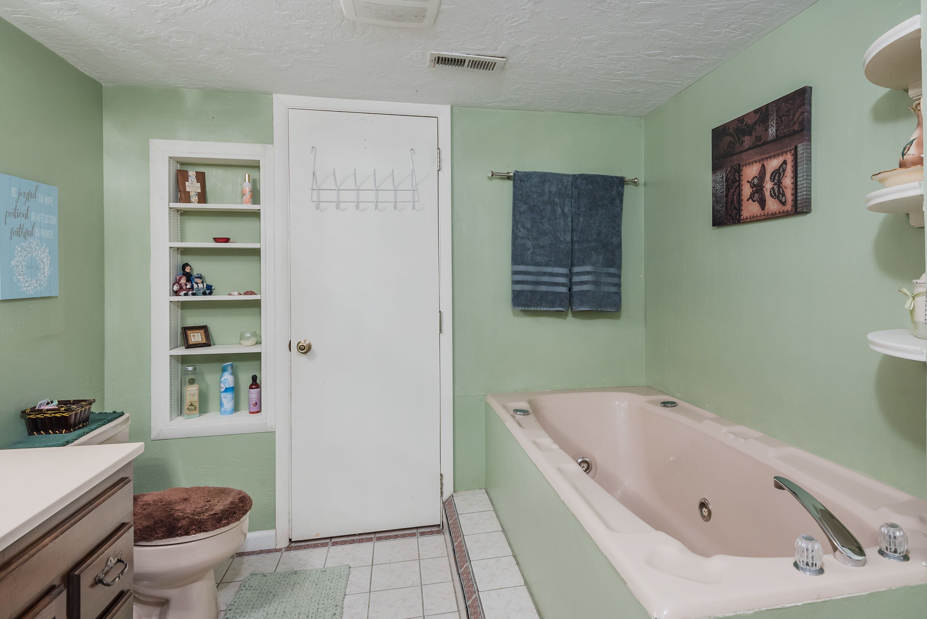 Een badkamer met een bad, toilet, planken en een deur.