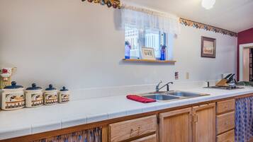 A kitchen with a white countertop, wooden cabinets, a sink, and a window with lace curtains.