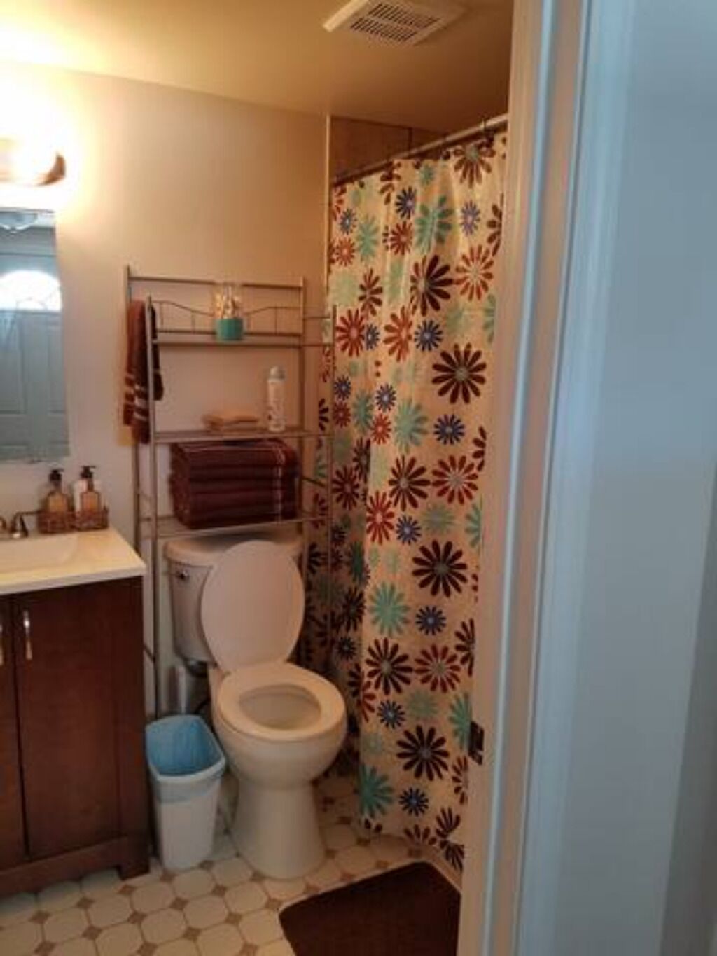 Un baño pequeño con inodoro, lavabo, cortina de ducha estampada con motivos florales y un cubo de basura.