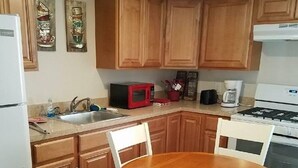 A compact kitchen with wooden cabinets, a round wooden table, and white chairs. - The Carters Wildwood Rentals-Suite #2 (Wildwood)