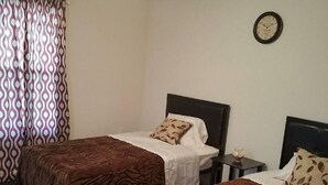 A hotel room with two single beds, a bedside table with a lamp, a clock on the wall, and a patterned curtain. - The Carters Wildwood Rentals-Suite #2 (Wildwood)