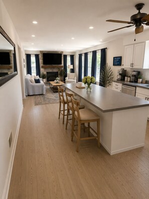 A modern kitchen with a central island, bar stools, a flat-screen TV, and a fireplace.