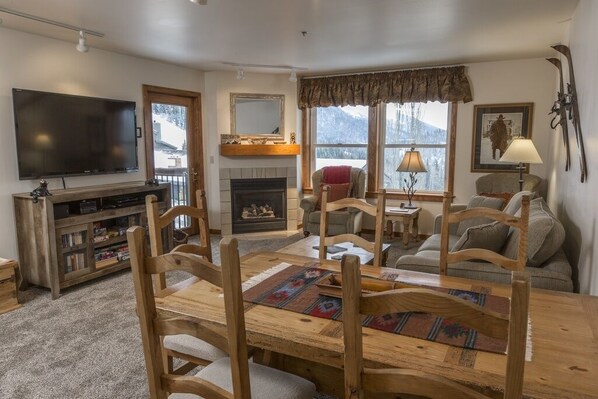 A cozy living room with a fireplace, a television, and a dining area with wooden furniture.