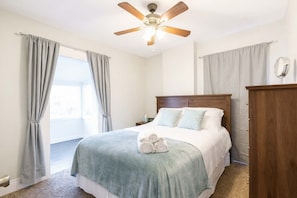 Un dormitorio con cama, cabecera de madera, ventilador de techo y mesita de noche con lámpara.