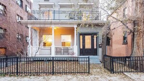 Ein zweistöckiges Reihenhaus mit Veranda, einer schwarzen Haustür und einem Balkon.