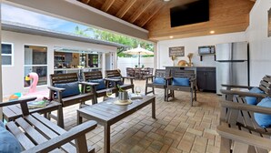 Eine Außenpatio mit Holzmöbeln, einer Küchenzeile und einem an der Wand montierten Fernseher.