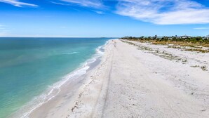 Ein weiter Sandstrand mit klarem, blauem Wasser und einigen Gebäuden in der Ferne.