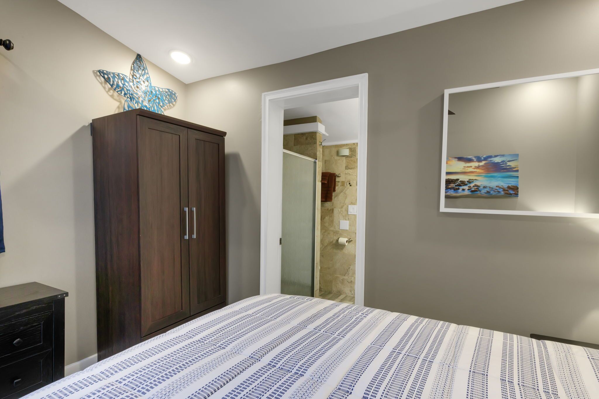 A bedroom with a bed, a wardrobe, a bathroom visible through an open door, and a framed picture on the wall.