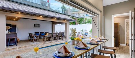 A dining area with a pool view, a bar, and a kitchen area.
