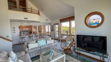 A spacious living area with a large TV, a dining area, and a kitchen.