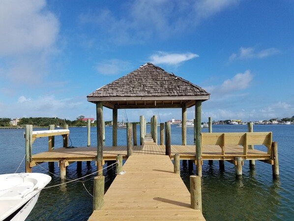 A wooden pier leading to a gazebo with a thatched roof, surrounded by calm water and a clear sky. - Pirate's Quay 3 South:  Incredible harbor views and sunsets. Docking. (Ocracoke)