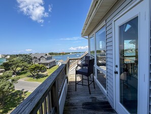 A wooden deck with a chair, overlooking a body of water and houses.