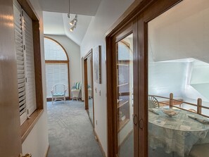 Un pasillo con una puerta de madera, una silla blanca y una mesa con mantel estampado.