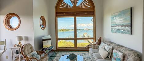 A living room with a large bay window, a view of a body of water, and a painting on the wall.