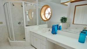 A modern bathroom with a glass-enclosed shower, a large mirror with a round wooden frame, and a white vanity with multiple drawers. - Pirate's Quay 3 South:  Incredible harbor views and sunsets. Docking. (Ocracoke)