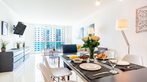 A modern dining area with a long table, chairs, and a view of a high-rise building. - Spacious condo w/ open layout across from the beach | WIFI + Parking (Sunny Isles Beach.)