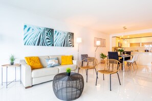A modern living room with a sofa, round coffee table, and chairs. There is a dining area with a table and chairs.