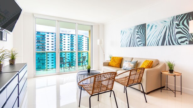 A modern living room with a sofa, two chairs, a coffee table, and a TV. - Spacious condo w/ open layout across from the beach | WIFI + Parking (Sunny Isles Beach.)