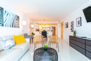 Un salon moderne avec un canapé blanc, deux fauteuils en rotin, une table basse en verre et un buffet en bois foncé.