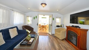 A living room with a blue sofa, a beige armchair, a wooden fireplace, and a television on the wall.