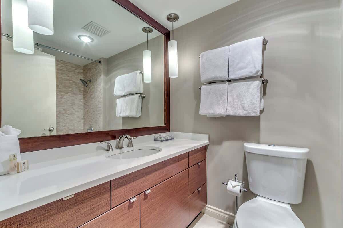 A modern bathroom with a large mirror, two sinks, a toilet, and hanging towels.