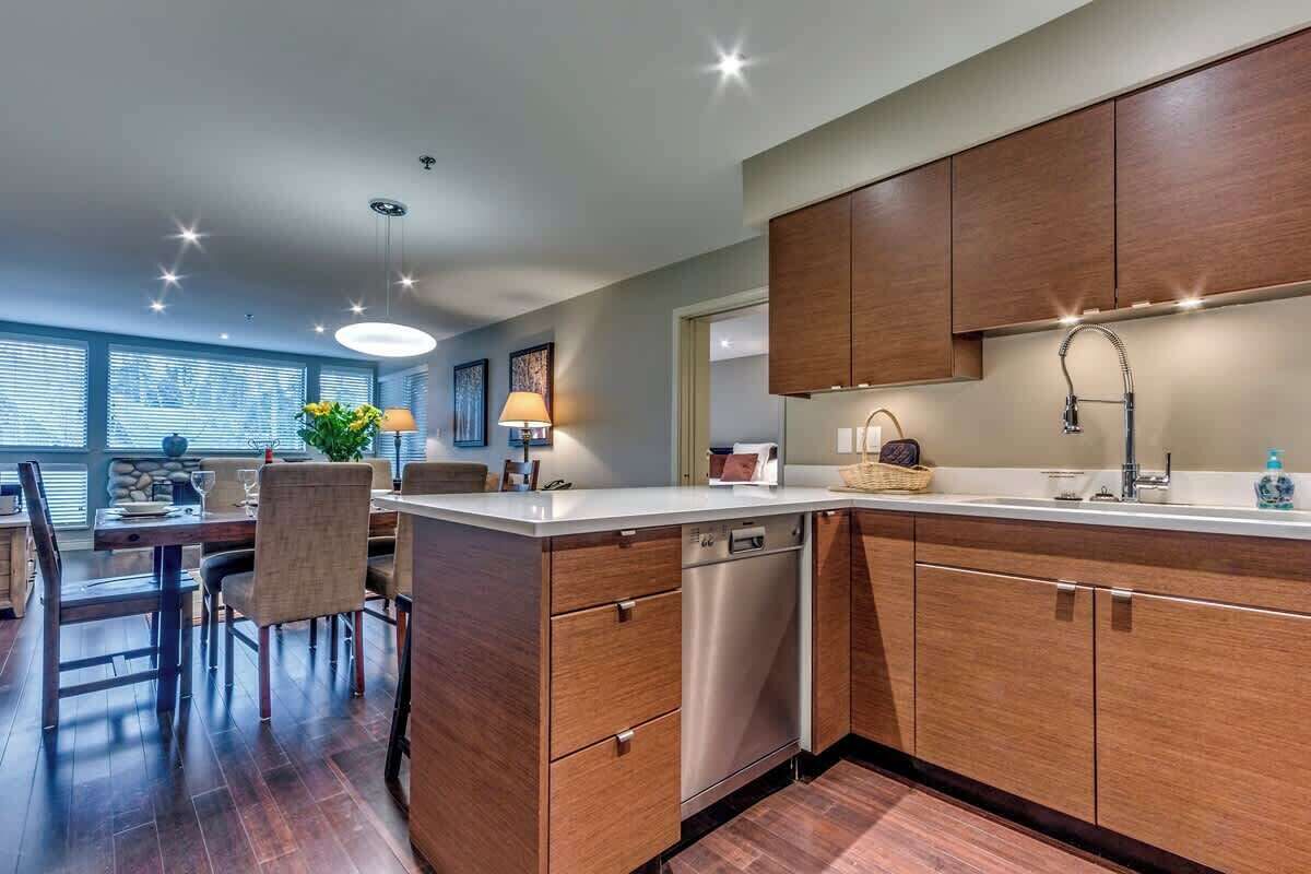 Una cocina moderna con armarios de madera, lavavajillas y un comedor con sillas y mesa.