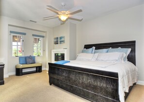 Ein Schlafzimmer mit einem großen Bett, einem Deckenventilator, einer Bank und einem Kamin.