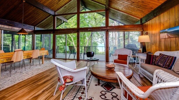 Une pièce spacieuse avec un plafond haut, de grandes fenêtres, un coin repas avec une table et des chaises, et un coin salon confortable avec un canapé et des fauteuils.