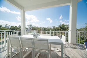 A covered outdoor dining area with a white table and chairs, surrounded by a white railing, overlooking a landscape with trees and a clear sky.