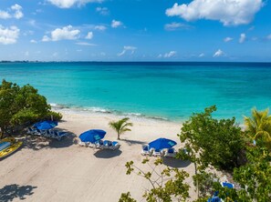 A beach with clear turquoise water, white sand, and blue umbrellas.