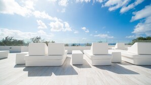 A rooftop terrace with white outdoor seating and a clear view of the sea.