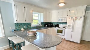 A kitchen with white cabinets, a granite countertop, a built-in oven, and a refrigerator. - Stranded On Purpose "Bluebird Day Too":  Spacious dog friendly with a pool table (Ocracoke)