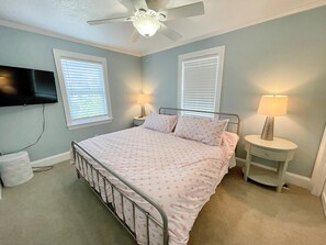 A bedroom with a bed, two bedside tables, a ceiling fan, and a TV mounted on the wall. - Stranded On Purpose "Bluebird Day Too":  Spacious dog friendly with a pool table (Ocracoke)