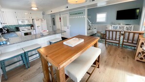 A modern kitchen with white cabinets, a granite countertop, and a wooden dining table with benches. - Stranded On Purpose "Bluebird Day Too":  Spacious dog friendly with a pool table (Ocracoke)