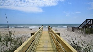 A wooden boardwalk leading to a beach with a wooden staircase on the right.