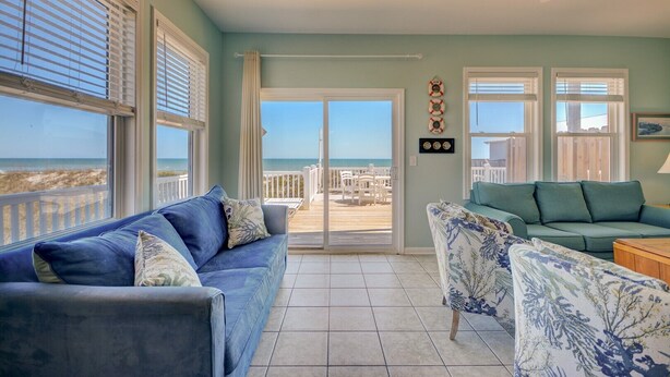 A room with a blue sofa, a patterned armchair, and a view of the beach through a sliding glass door.