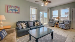 A spacious living room with a dark leather sofa, a matching armchair, a coffee table, and a ceiling fan. A large window provides a view of the outside.