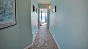 A hallway with light blue walls, carpeted floor, framed pictures, and a door leading to a balcony.