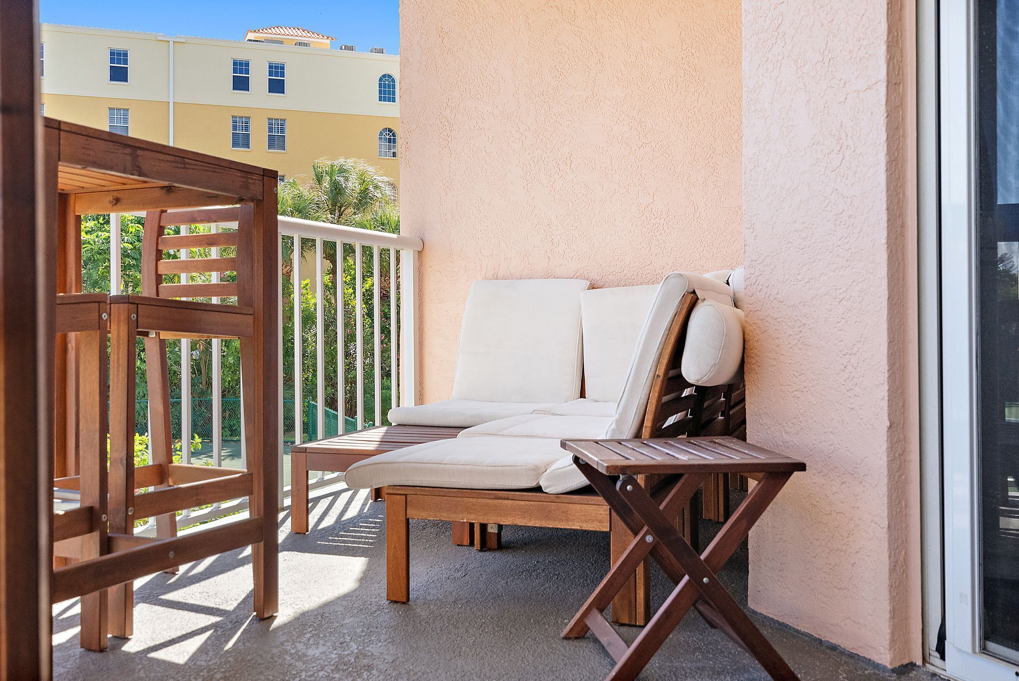 A balcony with a wooden chair and a sofa, a wooden pergola, and a view of buildings in the background.